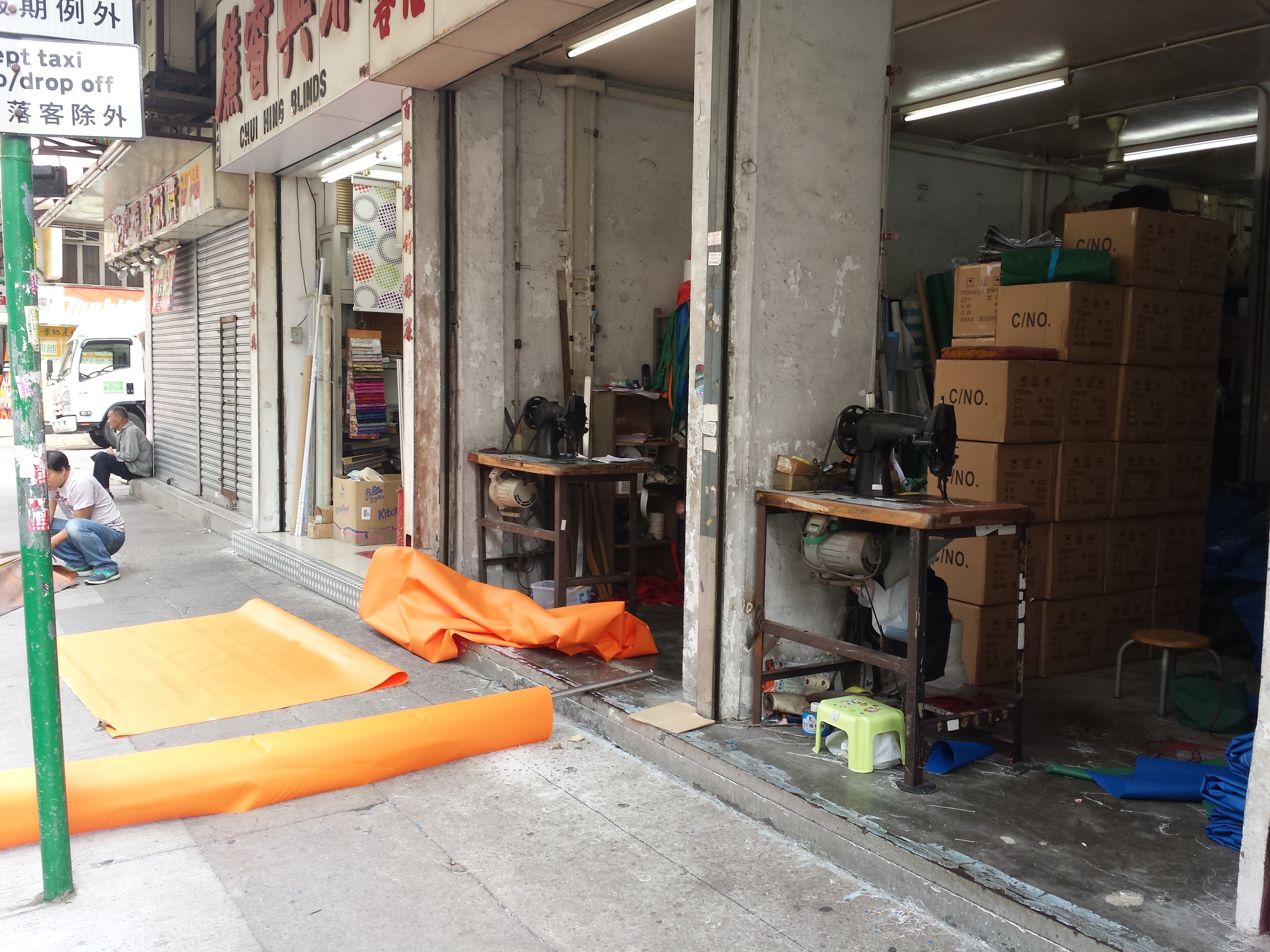 A Hong Kong street-level shop with orange canvas rolls and sewing machines on the pavement