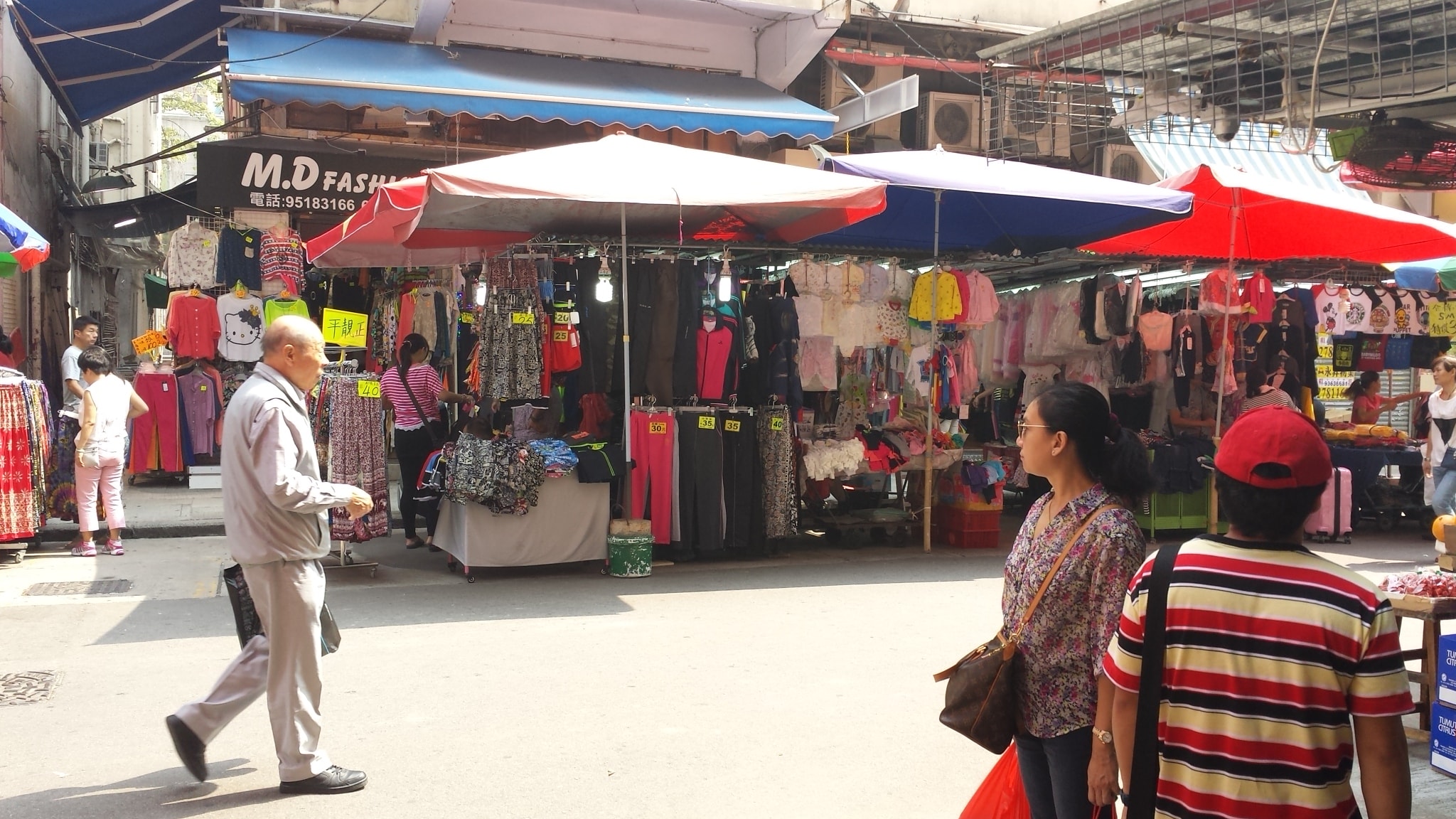 Clothing stalls with colourful garments under large umbrellas at a Hong Kong street market